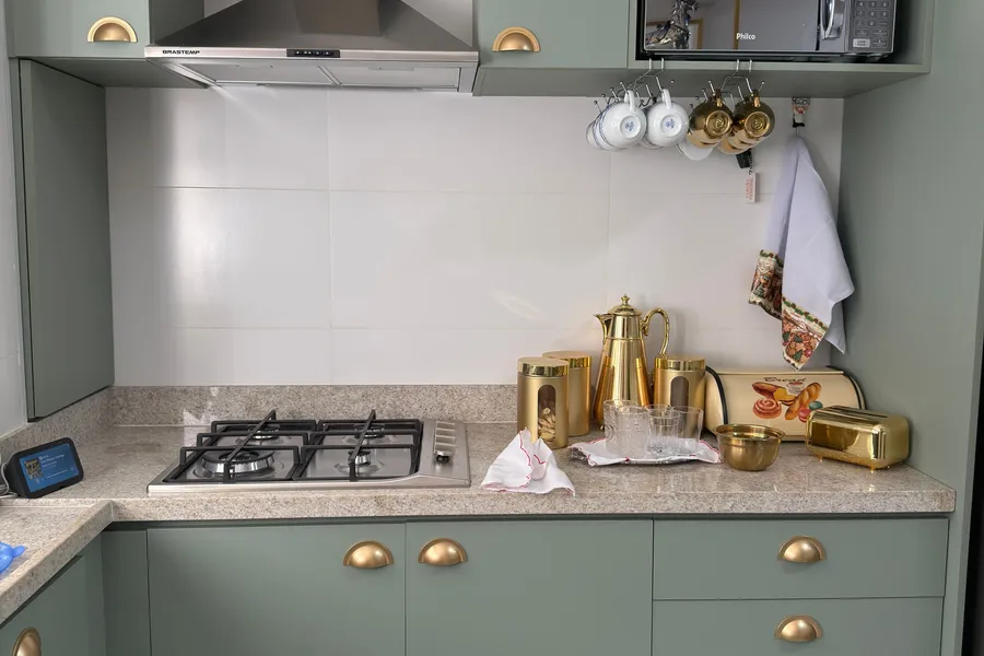 Sage-green kitchen cabinets with brass hardware beside a range hood and stone countertop.