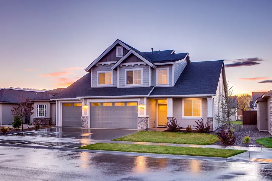 A two-story suburban home with painted siding, trim and garage doors, photographed at dusk with the windows lit.