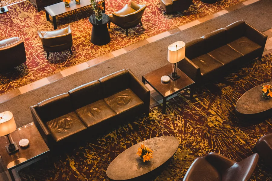 A warmly lit hospitality lounge seen from above, with lounge chairs and low tables on a patterned floor.