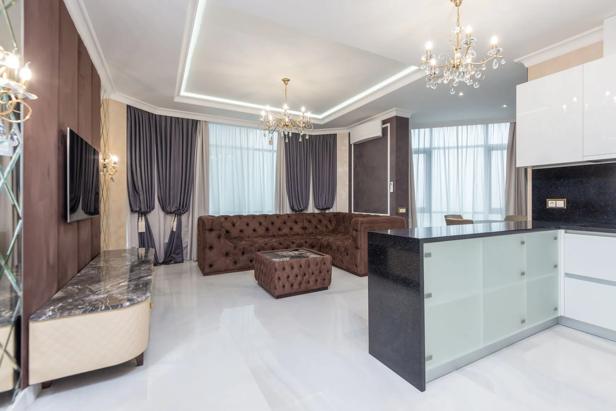 An open-plan living room with freshly painted walls, ceiling and trim in warm neutral tones, lit by a chandelier.