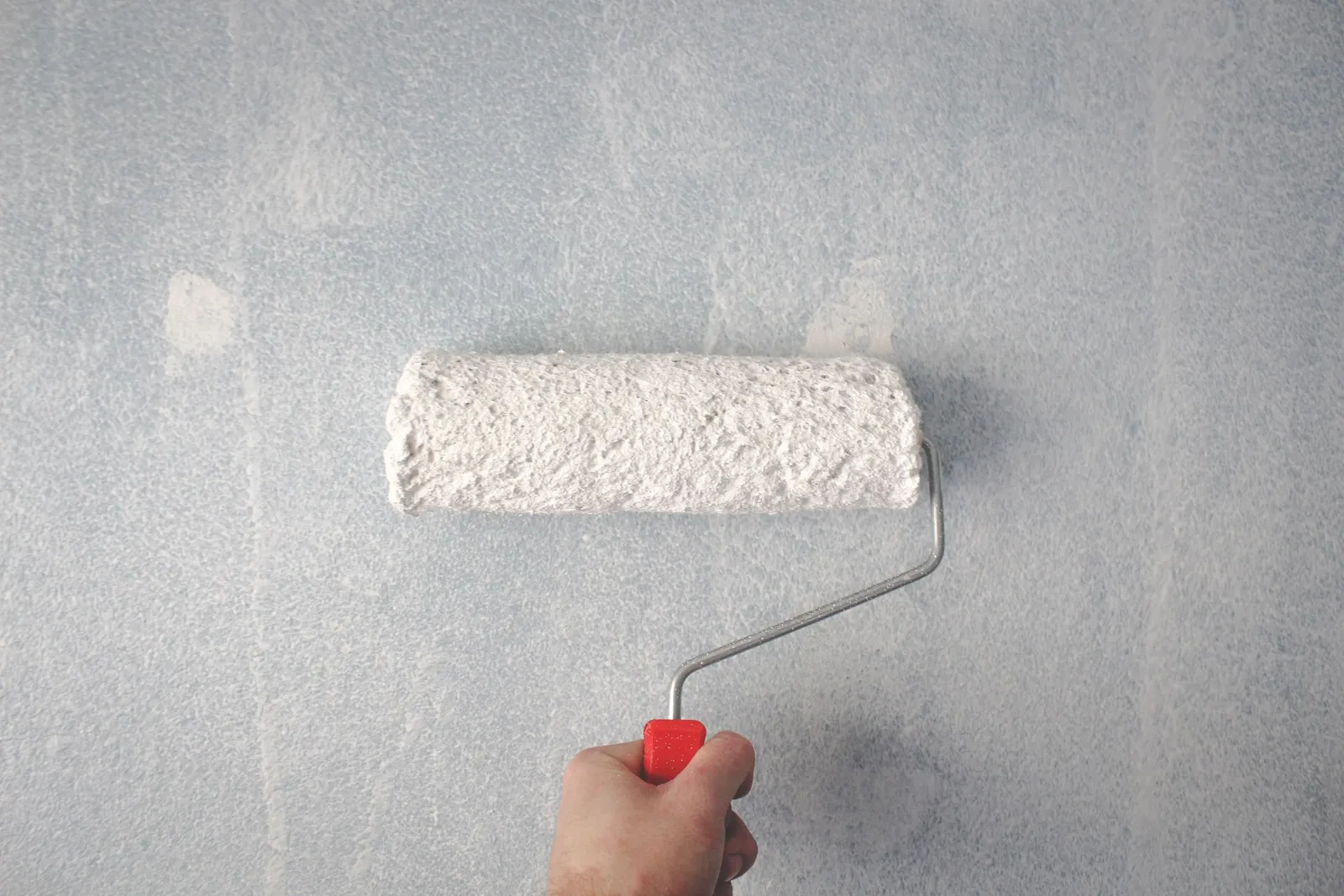 A hand rolling an even coat of pale paint across a smooth interior wall.