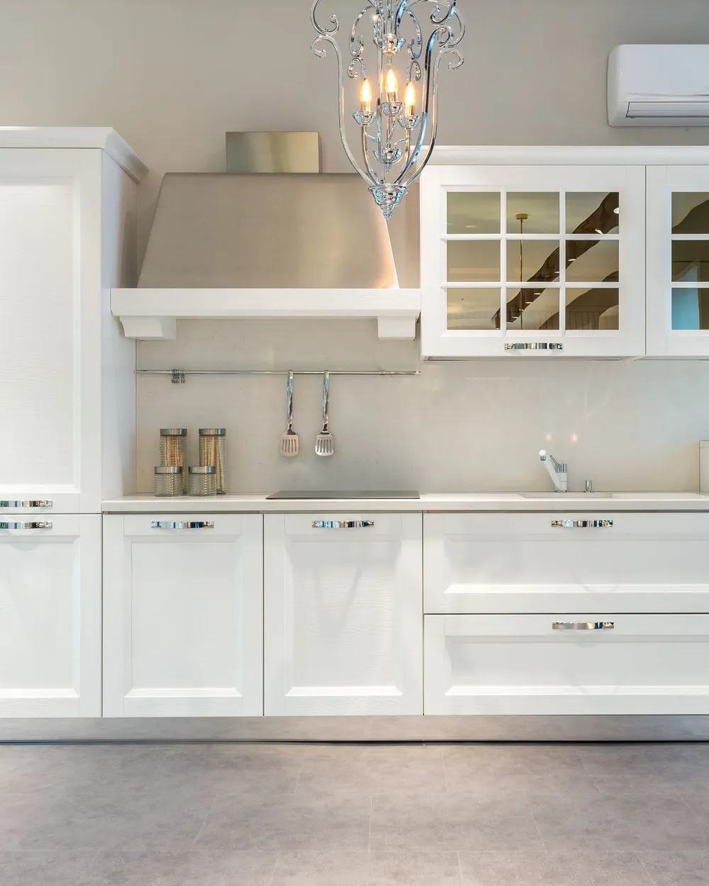 A kitchen with white shaker-style cabinets, glazed upper doors and a chandelier above the run of units.