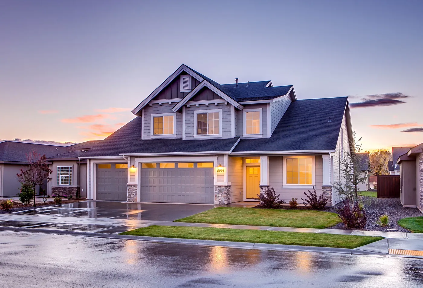 A two-story suburban house at dusk with painted siding, white trim, a covered porch and lit windows.