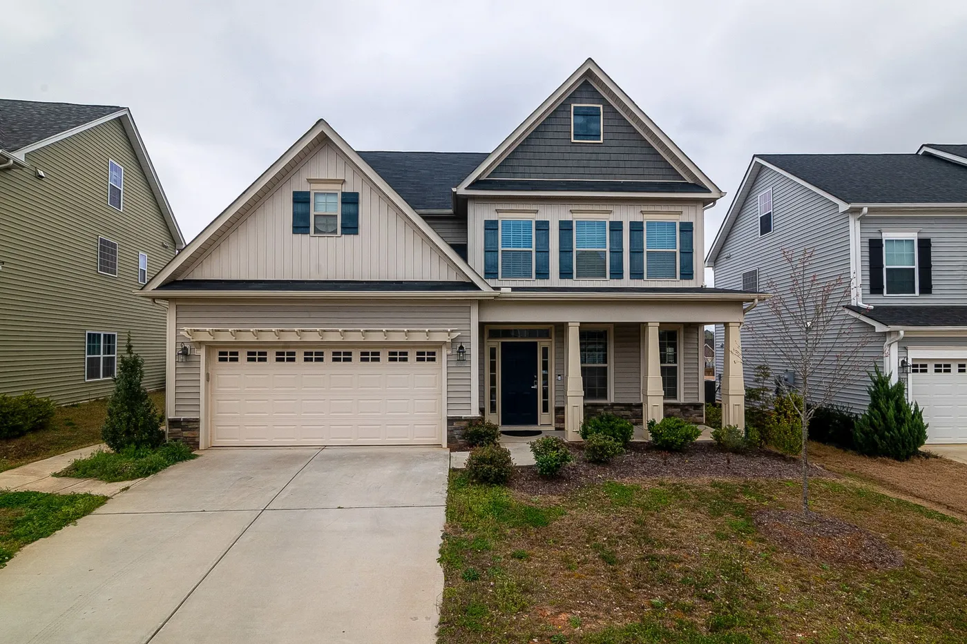 A suburban home with pale siding, contrasting shutters, white trim and a two-car garage door.