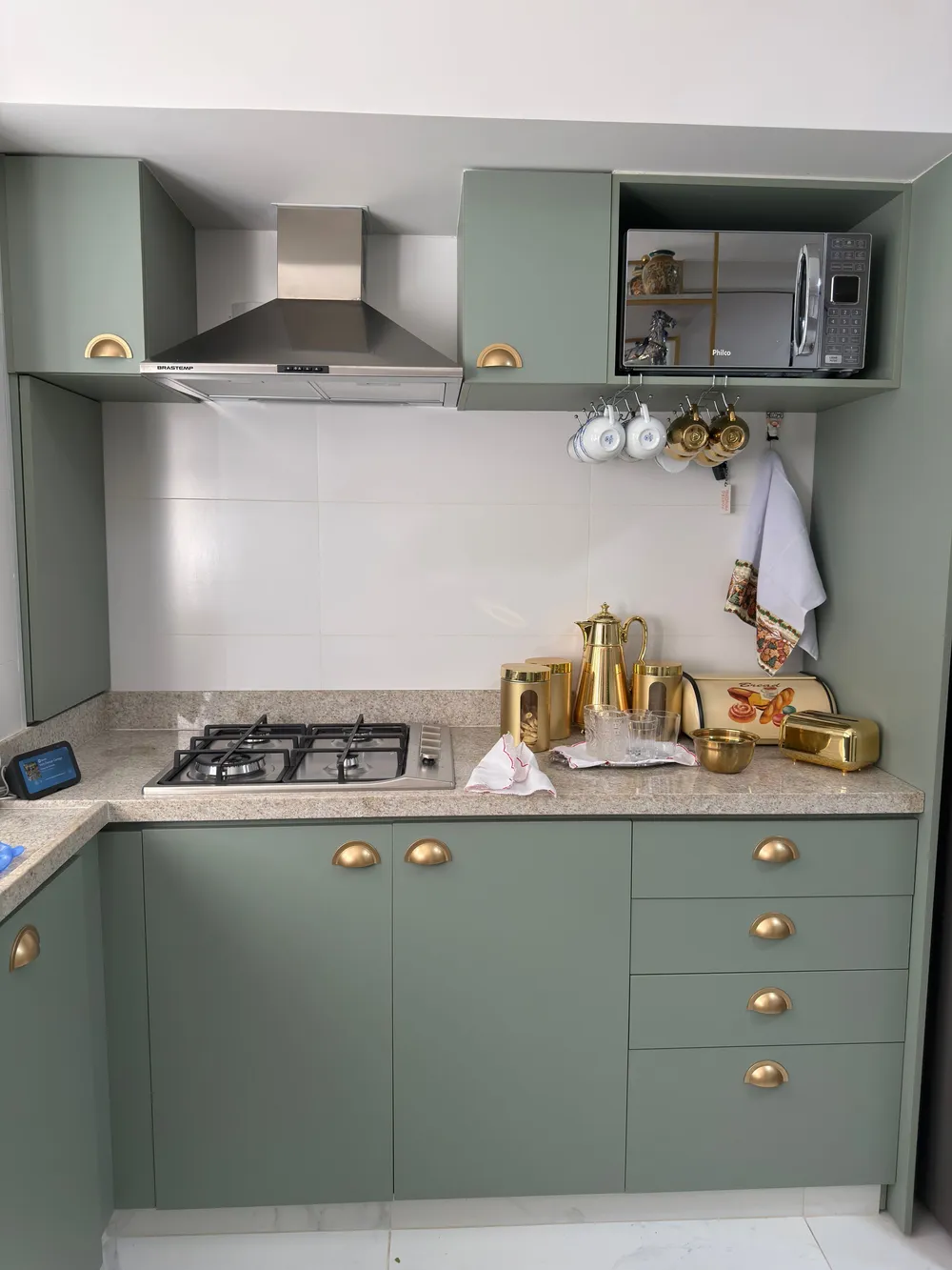 Sage-green kitchen cabinets with brass handles and a matching painted range hood above a gas cooktop.