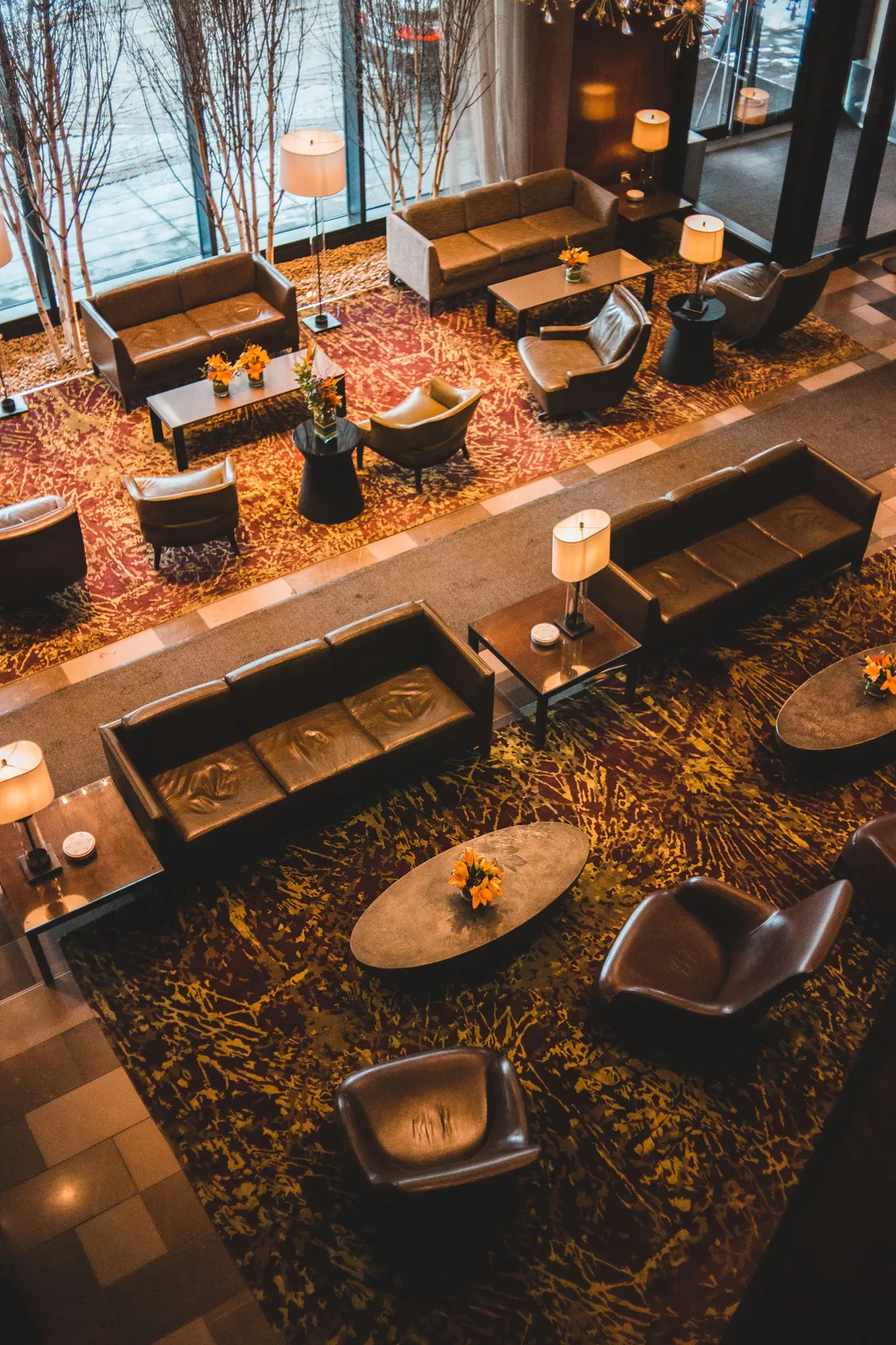 A warmly lit hospitality lounge photographed from above, with lounge chairs, low tables and a dark painted ceiling.
