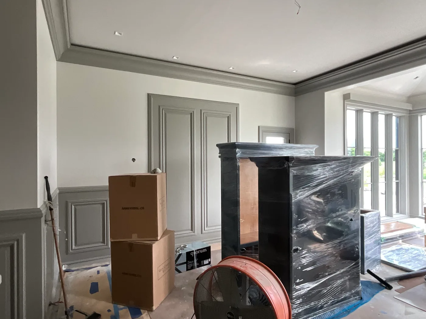An interior finished in soft gray with crown molding, raised-panel wainscoting and a pair of tall paneled doors painted to match, the floor papered and furniture wrapped in plastic.